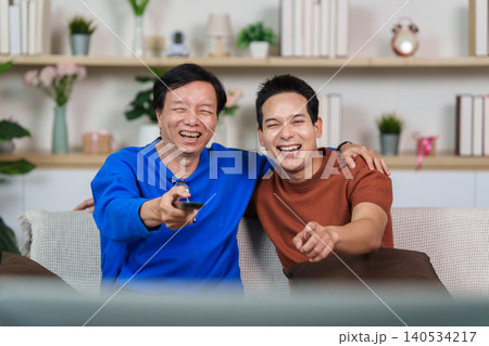 Happy Asian senior man and young man watching TV at home Happy Asian senior man and young man watching TV at home 140534217