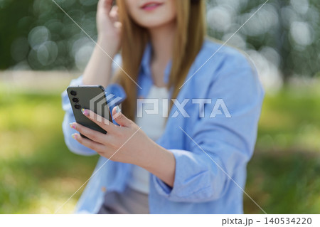 Asian woman in park using smartphone with headphones, digital lifestyle Asian woman in park using smartphone with headphones, digital lifestyle 140534220