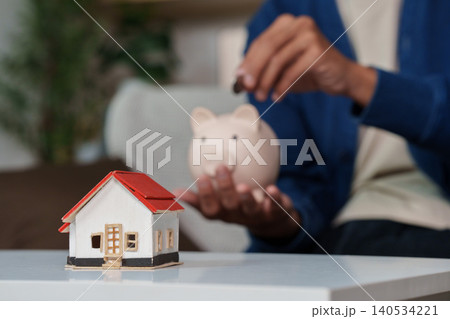 Asian man saving money in piggy bank for house investment Asian man saving money in piggy bank for house investment 140534221