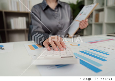 Asian woman professional doing finance analysis with calculator and charts in office 140534254