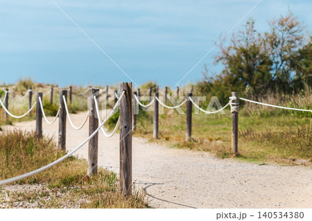 Rope lined walking trail crossing protected coastal dunes toward Mediterranean shoreline in Les Madrigueres nature reserve near Sant Salvador Rope lined walking trail crossing protected coastal dunes toward Mediterranean shoreline in Les Madrigueres nature reserve near Sant Salvador 140534380