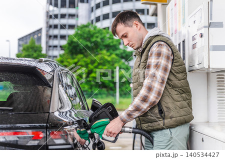 Young man refueling black car at urban gas station on rainy day in Germany Young man refueling black car at urban gas station on rainy day in Germany 140534427
