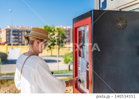 Young woman paying for parking at automated ticket machine in seaside resort, using self service payment terminal Young woman paying for parking at automated ticket machine in seaside resort, using self service payment terminal 140534551
