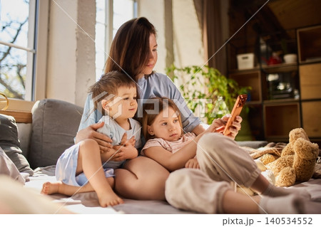Mother relaxing with children on sofa while using smartphone in cozy interior. Mother relaxing with children on sofa while using smartphone in cozy interior. 140534552