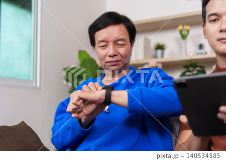 Asian senior man checking smartwatch for health monitoring with younger man Asian senior man checking smartwatch for health monitoring with younger man 140534585