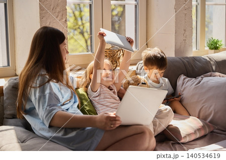 Mother with children using laptop and tablet together on sofa in bright living room. Mother with children using laptop and tablet together on sofa in bright living room. 140534619