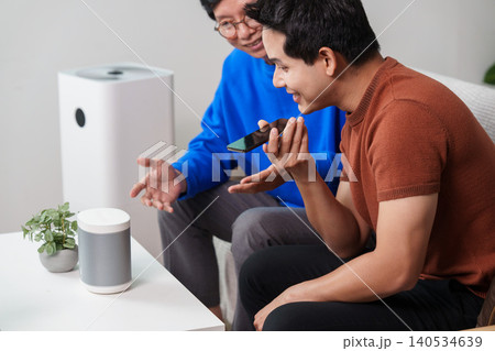 Asian senior and young man using smart home voice assistant at home Asian senior and young man using smart home voice assistant at home 140534639