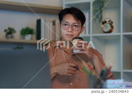 East Asian man focused on online meeting with laptop and coffee cup at night 140534643