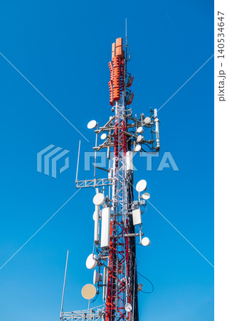 Cellular communication tower with multiple antennas and microwave dishes against clear blue sky, modern telecommunications infrastructure Cellular communication tower with multiple antennas and microwave dishes against clear blue sky, modern telecommunications infrastructure 140534647