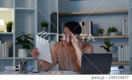 Stressed East Asian man thinking about problem while working late on laptop Stressed East Asian man thinking about problem while working late on laptop 140534657