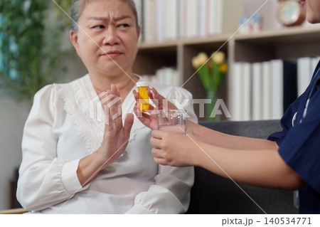 Senior woman refusing medication offered by caregiver Senior woman refusing medication offered by caregiver 140534771