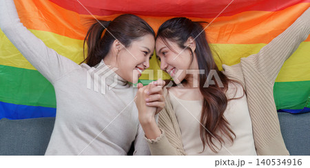 Asian lesbian couple holding hands, intimate moment with rainbow pride flag 140534916