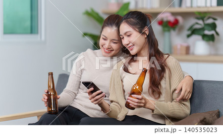 Asian women friends relaxing at home with smartphone and beer Asian women friends relaxing at home with smartphone and beer 140535023