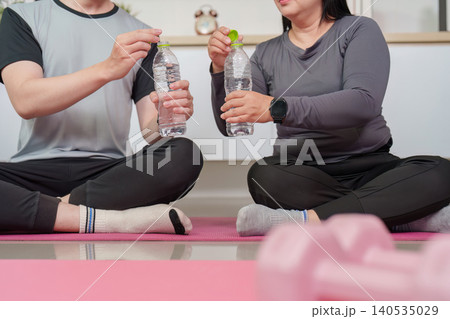 Two Asian people drinking water for hydration after home exercise workout Two Asian people drinking water for hydration after home exercise workout 140535029