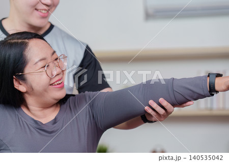 Asian woman doing physical therapy exercise with male trainer at home Asian woman doing physical therapy exercise with male trainer at home 140535042