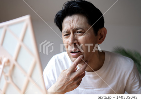 鏡を見ながら口元にできた口唇ヘルペスの症状に悩み、顔をしかめるミドル男性 鏡を見ながら口元にできた口唇ヘルペスの症状に悩み、顔をしかめるミドル男性 140535045