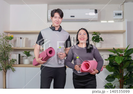 Asian couple holding yoga mats and water bottles after home workout Asian couple holding yoga mats and water bottles after home workout 140535099