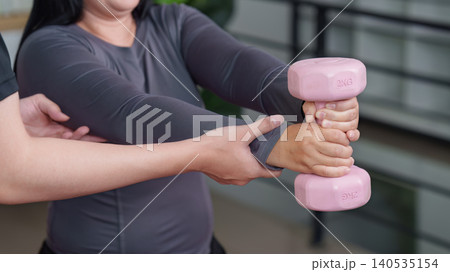 Asian woman doing weight training with pink dumbbell and male trainer at home 140535154