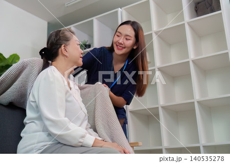 Asian caregiver helping senior woman with blanket in home living room Asian caregiver helping senior woman with blanket in home living room 140535278