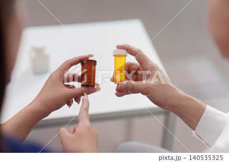 Doctor and patient comparing different medication pill bottles for treatment Doctor and patient comparing different medication pill bottles for treatment 140535325