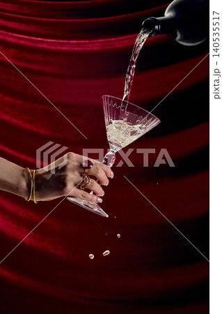 Close up pouring champagne into crystal cocktail glass with splash on red velvet background dramatic luxury drink scene Close up pouring champagne into crystal cocktail glass with splash on red velvet background dramatic luxury drink scene 140535517