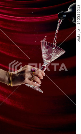 Elegant hand holding crystal martini glass while pouring champagne on red velvet background luxury drink concept Elegant hand holding crystal martini glass while pouring champagne on red velvet background luxury drink concept 140535518