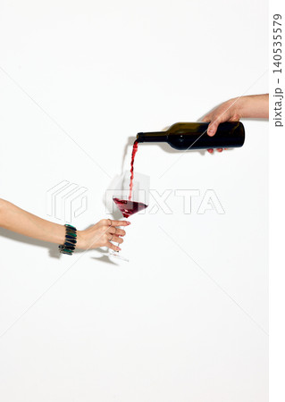 Hand holding wine glass while pouring red wine from bottle isolated on white 140535579