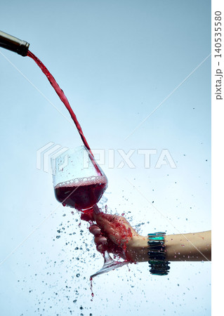 Close up red wine stream filling glass with splashes isolated on blue background 140535580