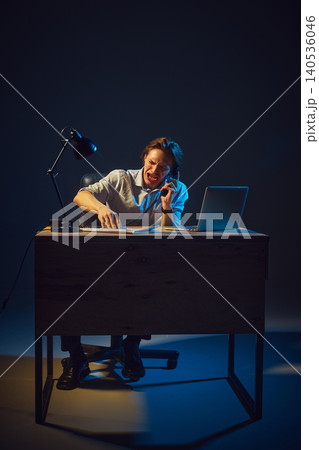 Man shouting on phone while working at desk in dramatic studio lighting. 140536046