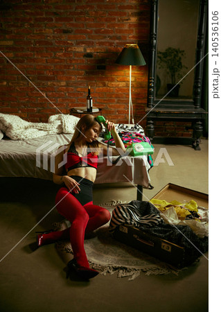Tired woman sitting on floor holding vintage phone near suitcase in loft bedroom Tired woman sitting on floor holding vintage phone near suitcase in loft bedroom 140536106