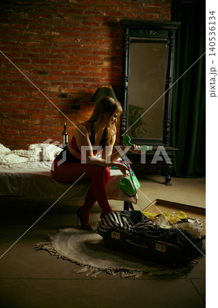Woman sitting on bed holding vintage phone looking down in moody loft bedroom interior. Woman sitting on bed holding vintage phone looking down in moody loft bedroom interior. 140536134