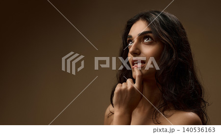 Thoughtful brunette woman touching glossy lips with natural wavy hair on brown background Thoughtful brunette woman touching glossy lips with natural wavy hair on brown background 140536163