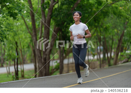 Smiling Black woman jogging on park path for outdoor fitness workout 140536218