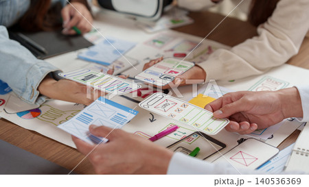 Cropped hands of designers comparing mobile app paper wireframes for UX UI prototyping 140536369