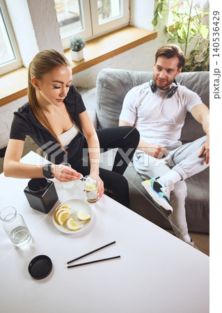 Top view of woman mixing supplement in lemon water before workout while man resting indoors Top view of woman mixing supplement in lemon water before workout while man resting indoors 140536429