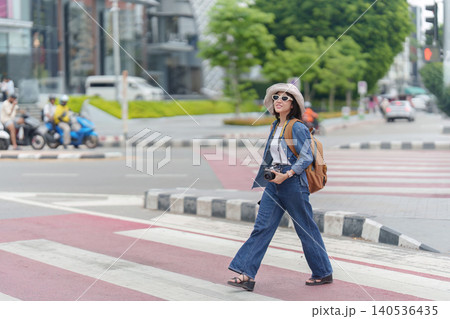Asian woman tourist walking on urban crosswalk with camera for city exploration and summer travel 140536435