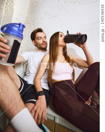 Close up of athletic couple resting and drinking protein shakes after workout indoors. Close up of athletic couple resting and drinking protein shakes after workout indoors. 140536438