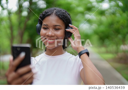 Happy Black woman enjoying music with headphones and smartphone outdoors for wellness lifestyle Happy Black woman enjoying music with headphones and smartphone outdoors for wellness lifestyle 140536439