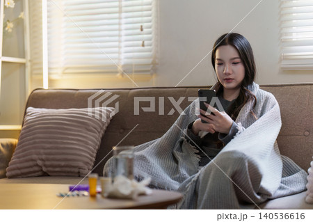Asian woman feeling unwell at home using smartphone for health information Asian woman feeling unwell at home using smartphone for health information 140536616