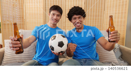 Two happy Asian men holding beer and soccer ball at home Two happy Asian men holding beer and soccer ball at home 140536621
