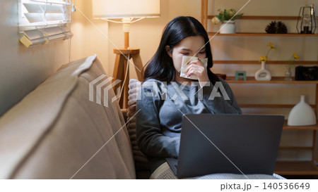 Asian woman blowing nose while working on laptop at home for remote work Asian woman blowing nose while working on laptop at home for remote work 140536649