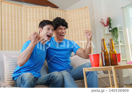 Excited Asian men cheering watching sports game at home Excited Asian men cheering watching sports game at home 140536909