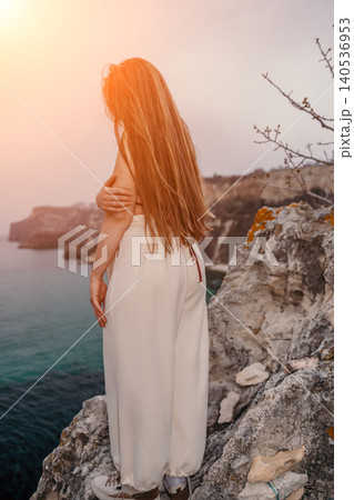 Woman sunset cliff overlooking the sea standing on a rocky edge with long hair during golden hour 140536953