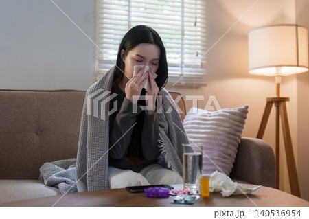 Asian woman blowing nose on sofa at home for cold and flu symptoms Asian woman blowing nose on sofa at home for cold and flu symptoms 140536954