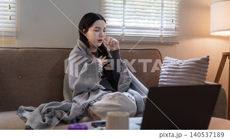 Asian woman coughing on sofa at home with laptop for remote work 140537189