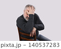 Stressed mature bearded man sitting on chair and holding head in frustration isolated on gray background 140537283