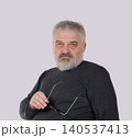 Mature bearded man holding eyeglasses and looking at camera 140537413