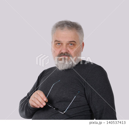 Mature bearded man holding eyeglasses and looking at camera Mature bearded man holding eyeglasses and looking at camera 140537413