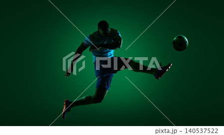 Soccer player kicking ball in dark green studio sport scene. Soccer player kicking ball in dark green studio sport scene. 140537522