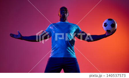Joyful soccer player holding ball with arms open on pink studio background. 140537573